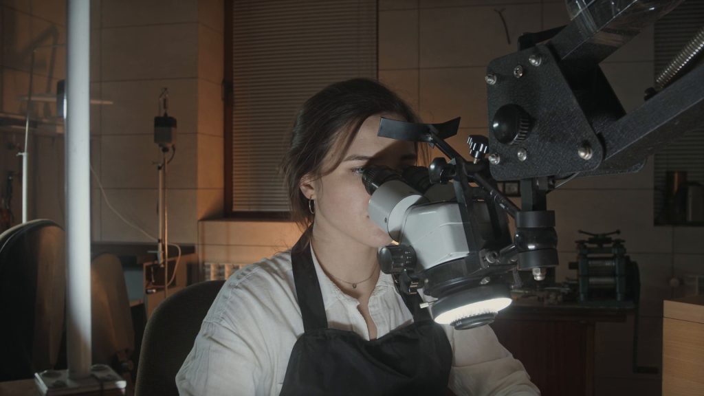 A jeweler working at the bench under a microscope