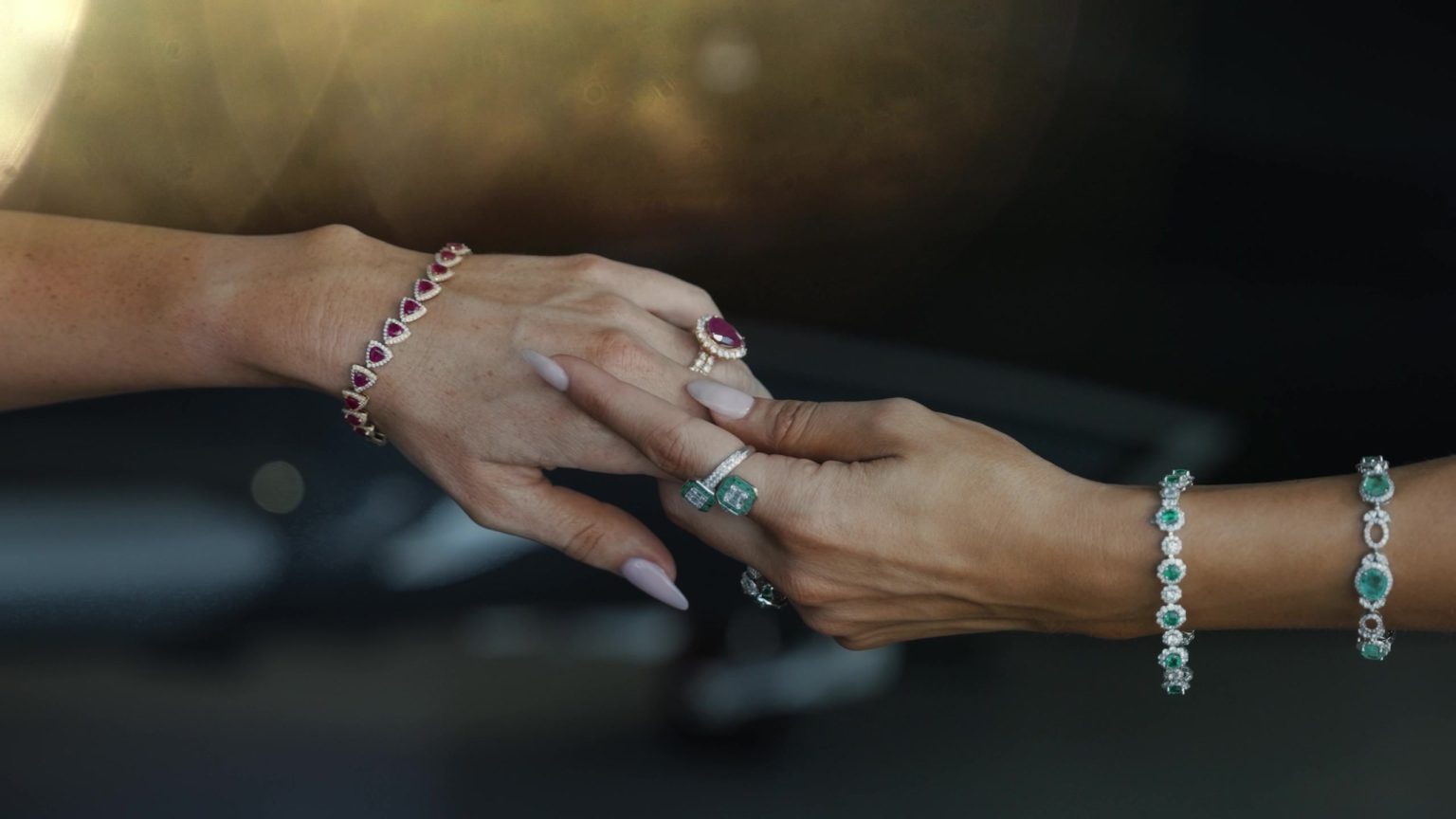 Hands wearing ruby and emerald rings and bracelets from Isaac Jewelers